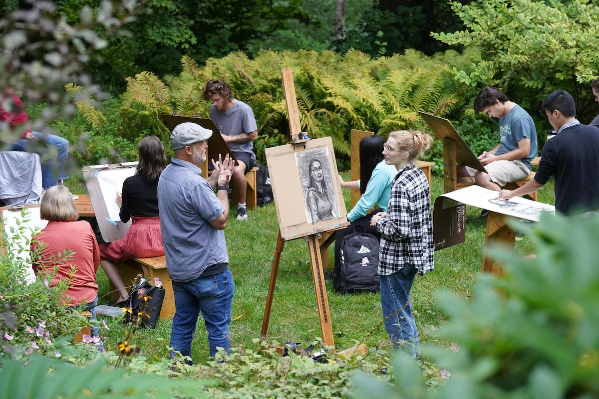 students with easles work on art outside in green grassy area